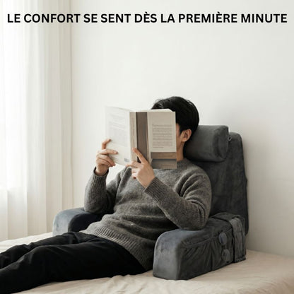 Personne semi-allongée sur un lit, adossée à un coussin de lecture ergonomique à mémoire de forme, en train de lire un livre dans une chambre épurée à la lumière naturelle.